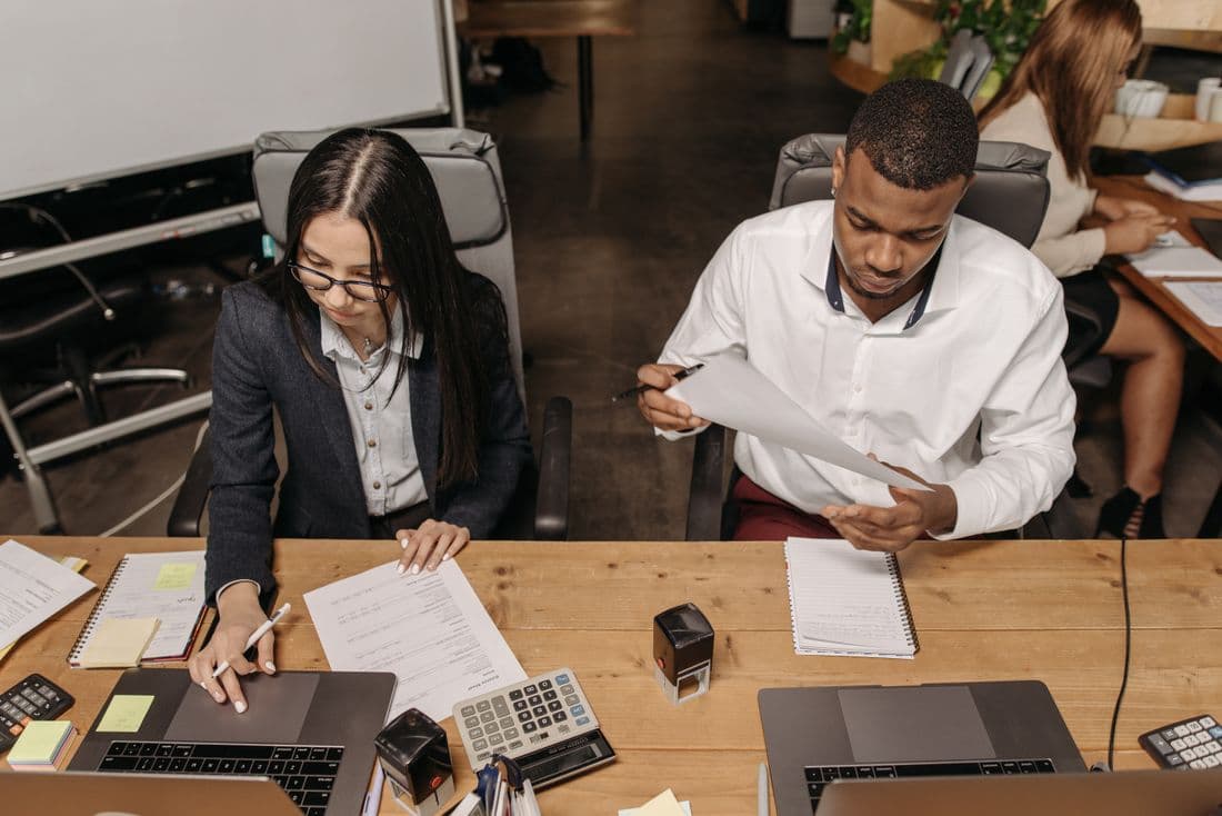 Two bookkeepers working through documents and calculators at a shared desk