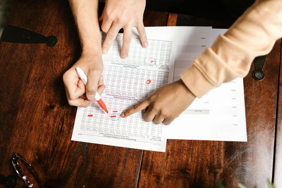 Two people marking up a financial statement in red pen