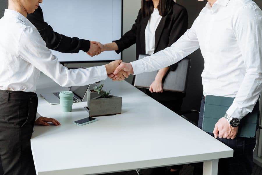 Two people shaking hands across a boardroom table after signing