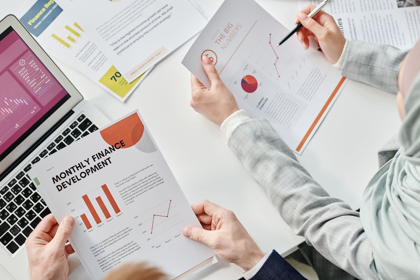 Two colleagues reviewing monthly finance reports and charts across a desk