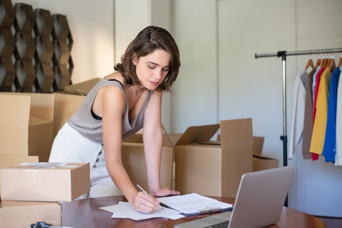 A shop owner packing orders beside a laptop and paperwork