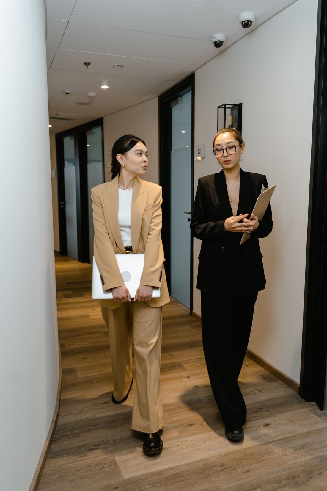 Two colleagues walking an office corridor, one carrying a clipboard